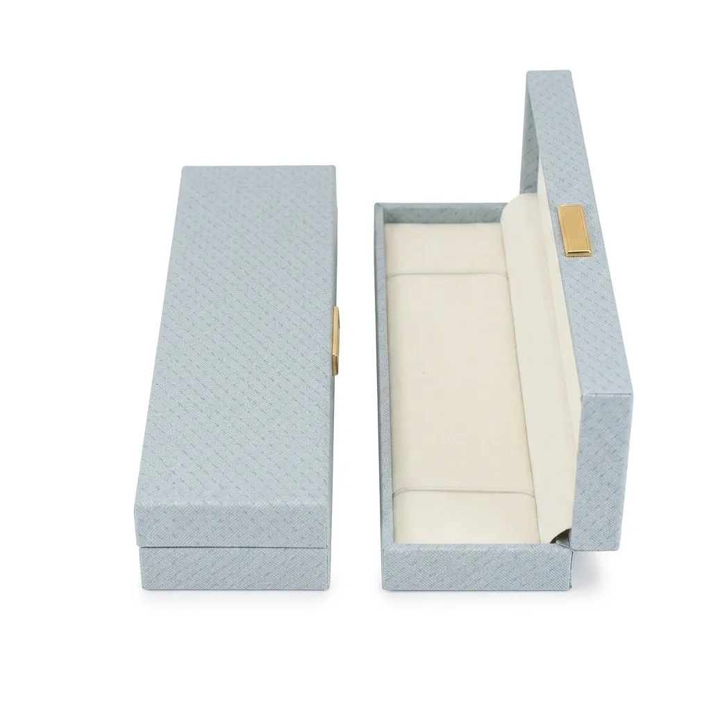 Empaque alargado en tono azul de 22,7 × 5 × 2,5 cm, ideal para cadenas, pulseras o accesorios lineales. Su diseño estilizado aporta distinción y una presentación más exclusiva.